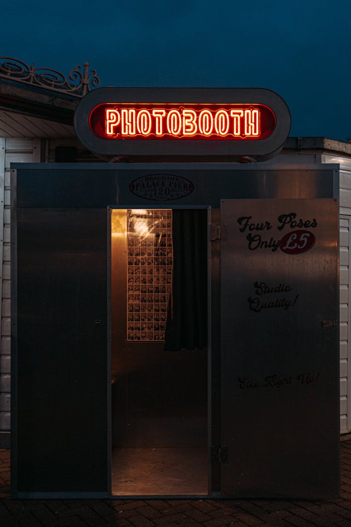 A neon-lit photobooth entrance captured against the night sky in Brighton, England.
